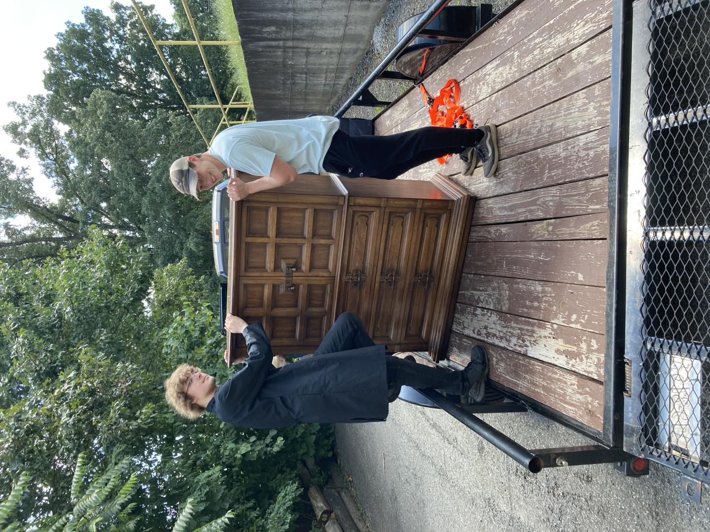 Two young men unloading a dresser from a utility trailer.