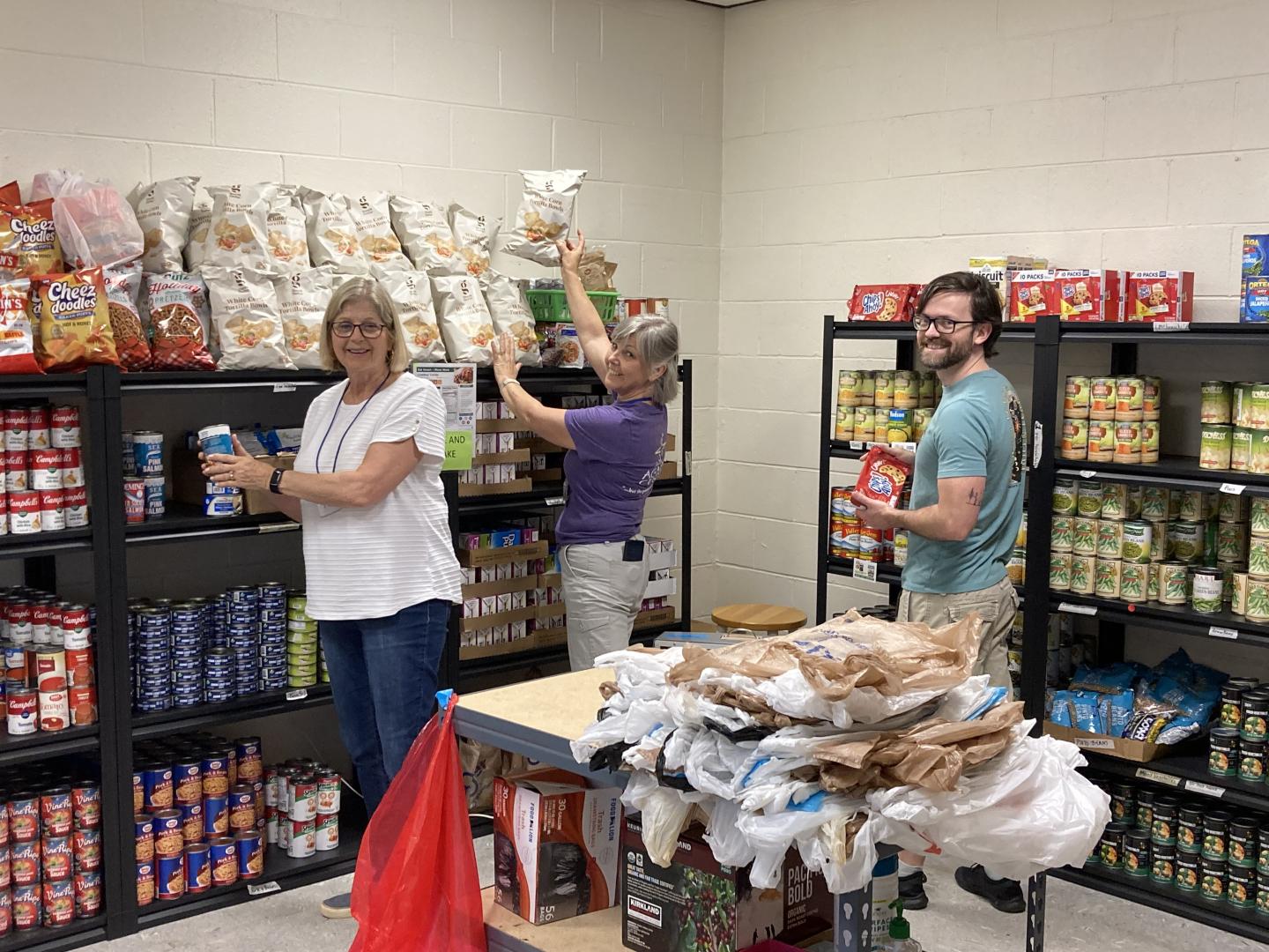 Three food pantry volunteers organizing food shelves.