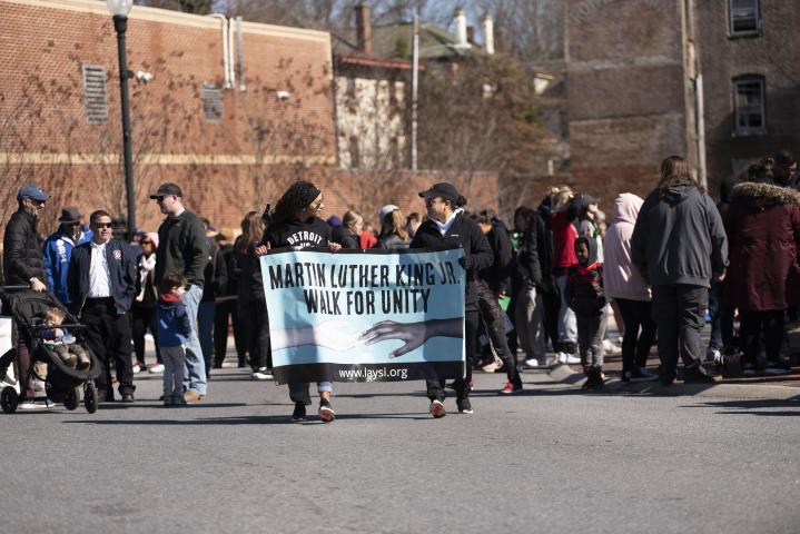 Image of a crowd walking towards the camera behind two women holding a banner that reads "Martin Luther King Jr. Walk for Unity"