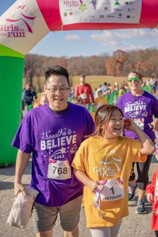 young girl and her father joyfully crossing the finish line at a race